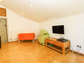 A living room with an orange sofa green bean bag wooden TV stand with a TV and gaming console at Llys Emrys in Beddgelert