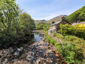 A river with rocks bordered by trees and a stone house near hills at Llys Emrys in Beddgelert