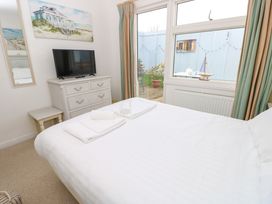 A bedroom with a bed with white linens towels on top a white dresser with a television a small side table and a large window with beige and green curtains at Plimoth N8 in Yarmouth
