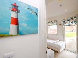 A bedroom with two single beds next to a window and glass door with floral curtains and a lighthouse painting on the wall at Plimoth N8 in Yarmouth