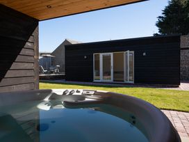 An outdoor hot tub on a patio with a view of a black wooden building with open white double doors at The Reef in Kessingland