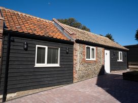 An exterior view of a single story building with black wood siding and pebble stone walls with white windows and a white door at Dunes Cottage in Kessingland