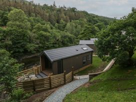 Two cabins near a river with trees in the background at Dubs Luxury Family Pod in Keswick