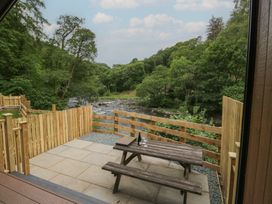 An outdoor area with a table and benches overlooking a river at Lingy Luxury Family Pod in Keswick