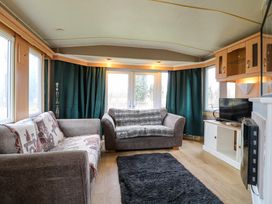 A living room with two sofas a black rug a TV on a white cabinet and green curtains at Beatrice's Static Caravan in Spalding