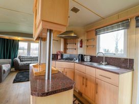 A kitchen with wooden cabinets a gas stove sink and countertop next to a living area with sofas and curtains at Beatrice's Static Caravan in Spalding