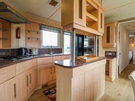 A kitchen with wooden cabinets a countertop a gas stove a kettle and a window at Beatrice's Static Caravan in Spalding