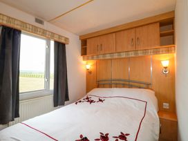 A bedroom with a double bed white bedding wooden cabinets and a window with dark curtains at Beatrice's Static Caravan in Spalding