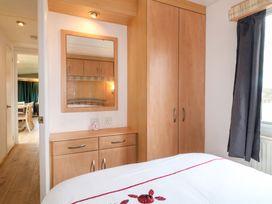A bedroom with a bed dresser wardrobe and a window with curtains at Beatrice's Static Caravan in Spalding