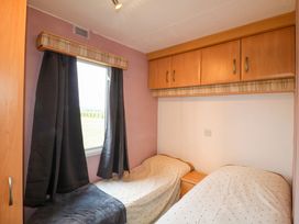 A bedroom with two single beds a window with dark curtains and overhead wooden cabinets at Beatrice's Static Caravan in Spalding