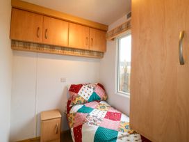A small bedroom with a single bed covered in a multicolored patchwork quilt beside a window and wooden cabinets at Beatrice's Static Caravan in Spalding