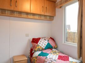 A bedroom with a single bed next to a window and wooden cabinets above at Beatrice's Static Caravan in Spalding