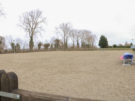 An empty enclosed outdoor arena with a sandy ground and trees in the background at Beatrice's Static Caravan in Spalding