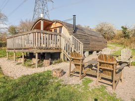 A wooden cabin with a deck and outdoor chairs on gravel surrounded by grass at Cabanau Bach in Bedwas