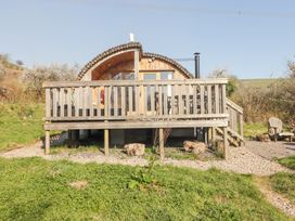 A wooden pod cabin with a deck and outdoor chairs on grass and gravel at Cabanau Bach in Bedwas