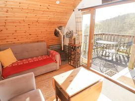 A small living room with a sofa a chair a coffee table a wood stove and a door leading to a balcony with a table and chairs at Cabanau Bach in Bedwas