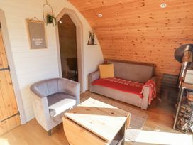 A seating area with a grey armchair a grey sofa with a red throw and a wooden coffee table in a room with wooden walls and a wood stove at Cabanau Bach in Bedwas