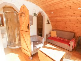 A small living room with a sofa a gray armchair a wooden table a wooden door leading to a bathroom with a glass shower at Cabanau Bach in Bedwas