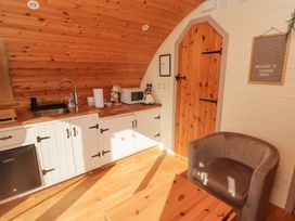 A kitchen area with a sink microwave kettle and paper towel next to a wooden door and a chair at Cabanau Bach in Bedwas