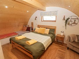 A bedroom with a double bed with pillows and folded towels a side table a chaise lounge and a wooden curved ceiling at Cabanau Bach in Bedwas
