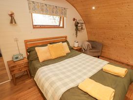 A bedroom with a double bed green bedding and yellow pillows beside a small wooden nightstand and a gray chair at Cabanau Bach in Bedwas