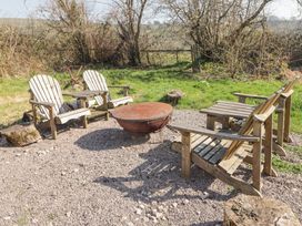 An outdoor seating area with four wooden chairs around a metal fire pit on gravel at Cabanau Bach in Bedwas