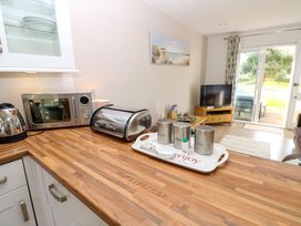 A kitchen countertop with a kettle microwave bread box and metal containers on a tray overlooking a living room with a television and sliding glass door at Plimoth N9 in Yarmouth