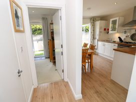 A hallway leading to a carpeted room with a TV and a kitchen with wooden floor and a dining table with chairs at Plimoth N9 in Yarmouth