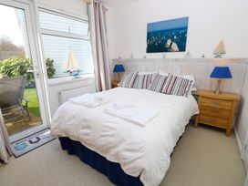 A bedroom with a double bed and striped pillows bedside tables with lamps and a door leading to a garden at Plimoth N9 in Yarmouth