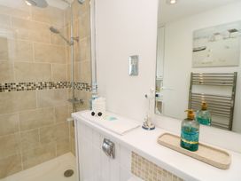 A bathroom with a tiled shower area a shelf with soap lotion and decorative items and a wall mirror at Plimoth N9 in Yarmouth