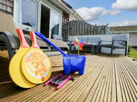 A wooden deck with a lounge chair beach paddles blue bucket and windmill next to outdoor seating at Plimoth N9 in Yarmouth