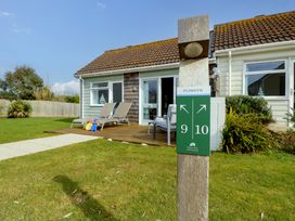 A cottage with two lounge chairs on a wooden deck and a sign post showing numbers 9 and 10 at Plimoth N9 in Yarmouth