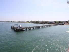 A long wooden pier extending into the water with boats in the distance and buildings along the shoreline at Plimoth N9 in Yarmouth