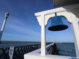 A blue bell hanging on a white wooden structure by a long pier extending into the sea at Plimoth N9 in Yarmouth