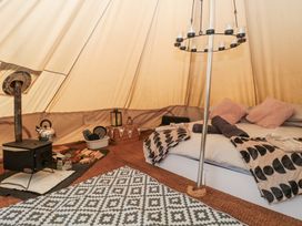 Interior of a tent with a bed with pillows and blankets a wood stove with kettle firewood and a patterned rug on the floor at Bell tent 1 Camerton near Timsbury