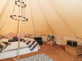 A bed with pillows and blankets inside a bell tent with wooden crates and a patterned rug at Bell tent 1 Camerton near Timsbury