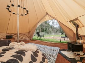 Interior of a bell tent with blankets on the floor a wood burning stove and two chairs outside at Bell tent 1 Camerton near Timsbury