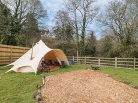 A bell tent with chairs and a wood chip fire pit area in a fenced grassy garden at Bell tent 1 in Camerton near Timsbury