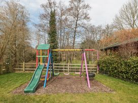 A playground with a slide and three swings surrounded by grass and trees at Bell tent 1 in Camerton near Timsbury