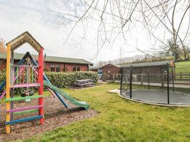 An outdoor play area with a colorful slide, swings, a picnic table, and a trampoline at Bell tent 1 in Camerton near Timsbury