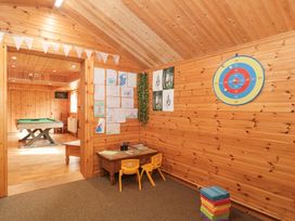 A wooden playroom with a small table and two yellow chairs children's drawings on the wall a dartboard and a stack of colorful blocks with a pool table in the adjacent room at Bell tent 1 in Camerton near Timsbury