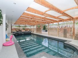 An indoor swimming pool with wooden beams on the ceiling and lattice screens with hanging plants at Bell tent 1 in Camerton near Timsbury
