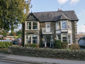 A stone house with bay windows and a small balcony behind a low stone wall with shrubs at Fir Trees in Windermere