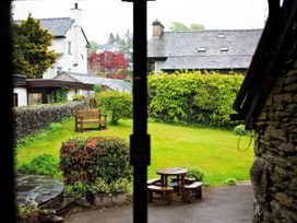 A garden with wooden bench and round wooden table with benches near a stone wall at Fir Trees in Windermere