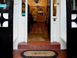 An entrance with black doors a welcome mat and a hallway with tiled floor and chandelier at Fir Trees in Windermere
