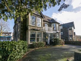 A stone building with large windows and a small balcony with bushes and trees in front at Fir Trees in Windermere