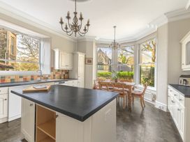 A kitchen with an island countertop dining table and chairs and large windows at Fir Trees in Windermere