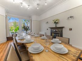 A dining room with a long wooden table set with white dishes and glassware and chairs around it at Fir Trees in Windermere