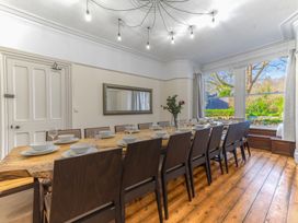 A dining room with a long wooden table surrounded by chairs and set with plates and glasses at Fir Trees in Windermere