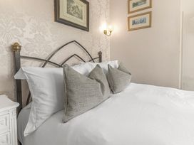 A bed with white sheets and three gray pillows against a floral wallpaper at Fir Trees in Windermere